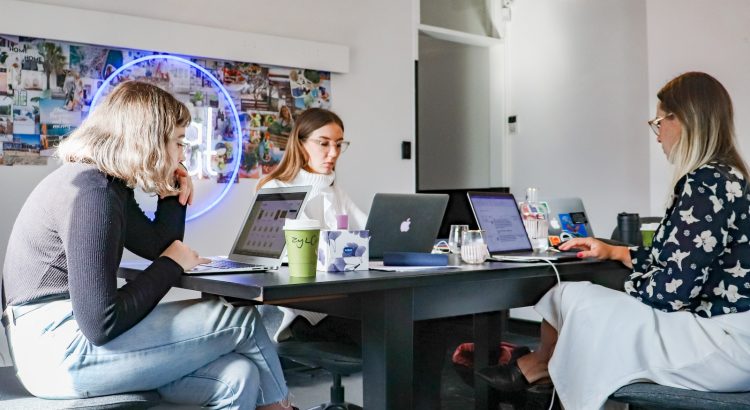 3 women sitting on chair in front of table with laptop computers